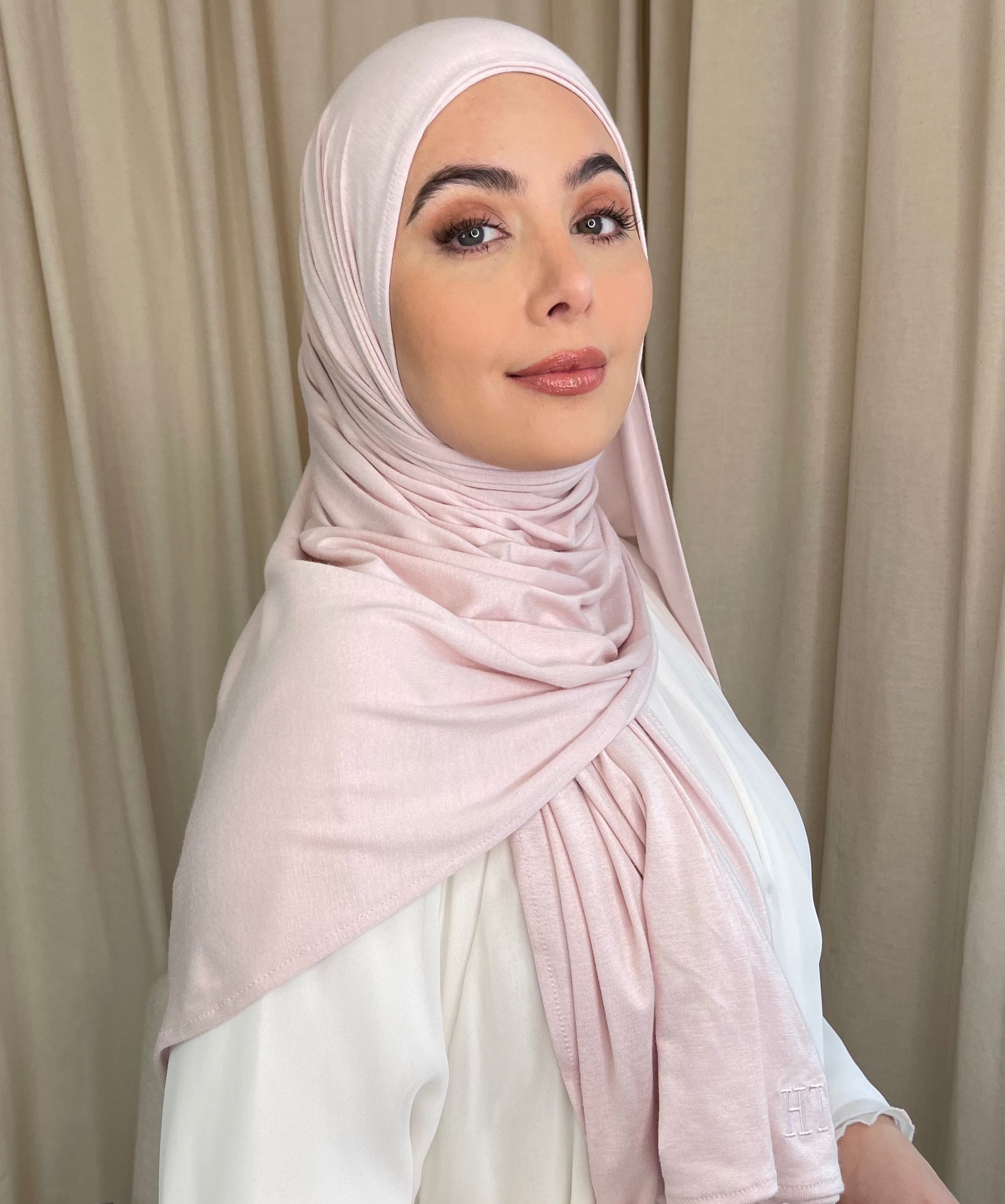A muslim woman wearing a light pink, lightweight jersey hijab, draped over the head and neck, full coverage hijab styles.