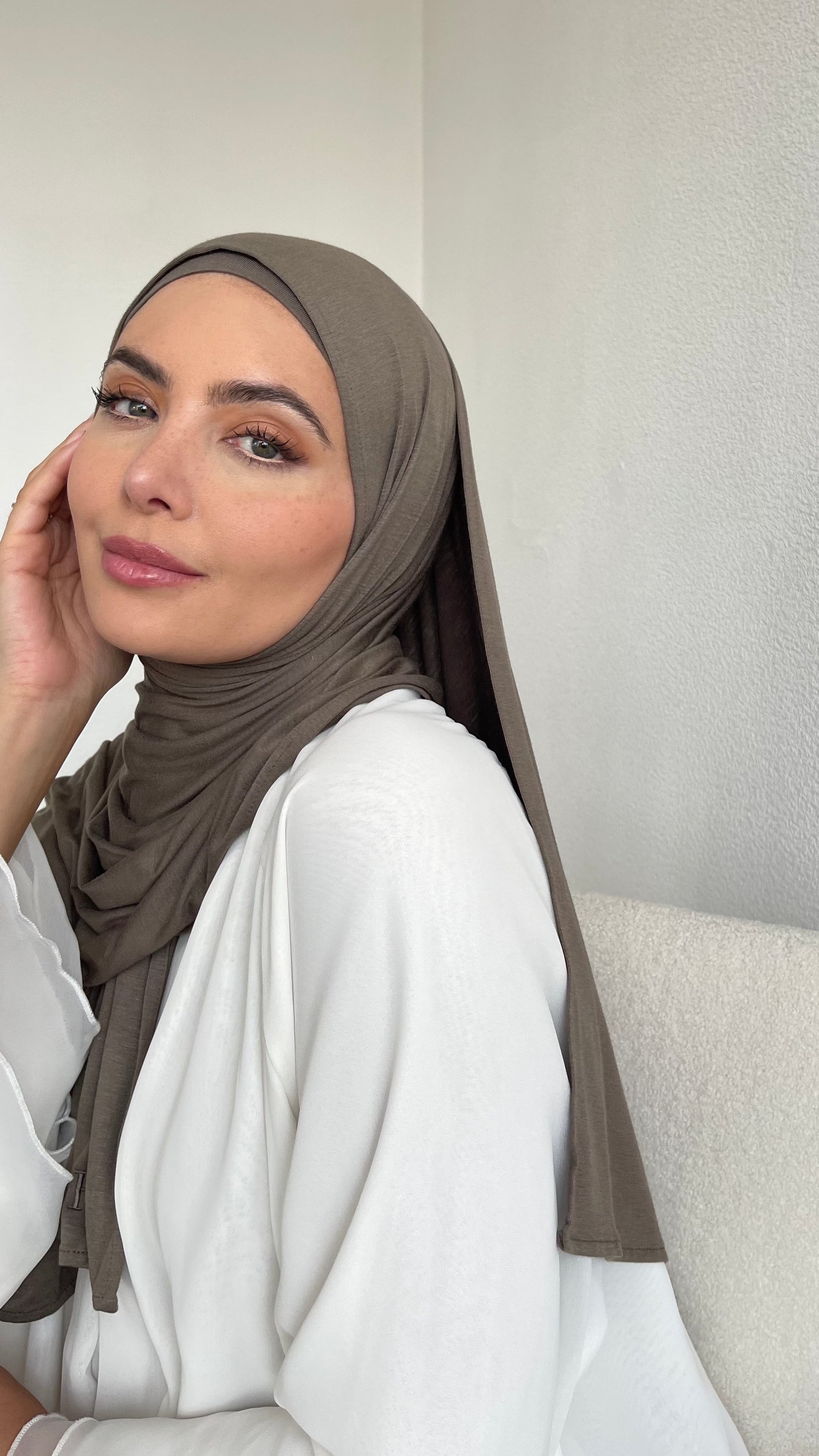 A muslim woman wearing a khaki green jersey hijab, paired with a white modest outfit look.