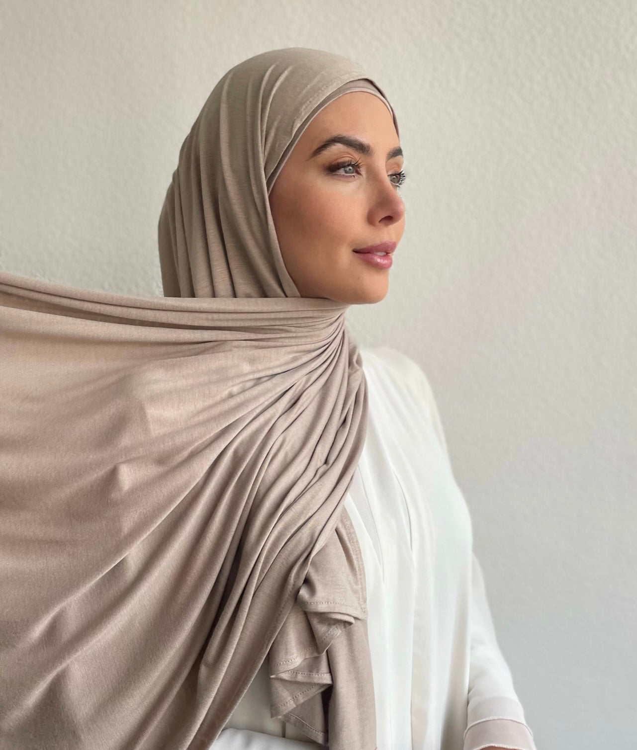 A woman wearing a beige jersey hijab, draped over the head and shoulders. Most popular hijab colour.