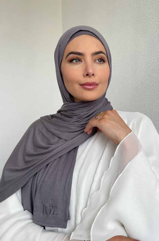 A hijabi woman wearing a grey premium lightweight jersey hijab, paired with a white abaya.