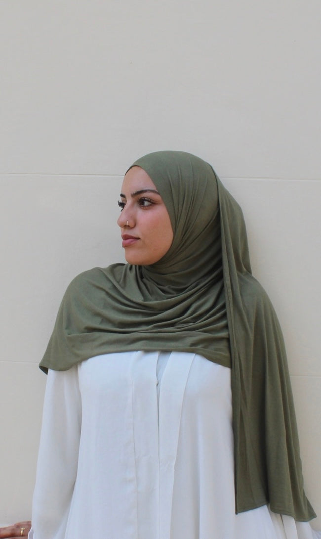 Woman wearing an olive green hijab against a plain background hijabi in london