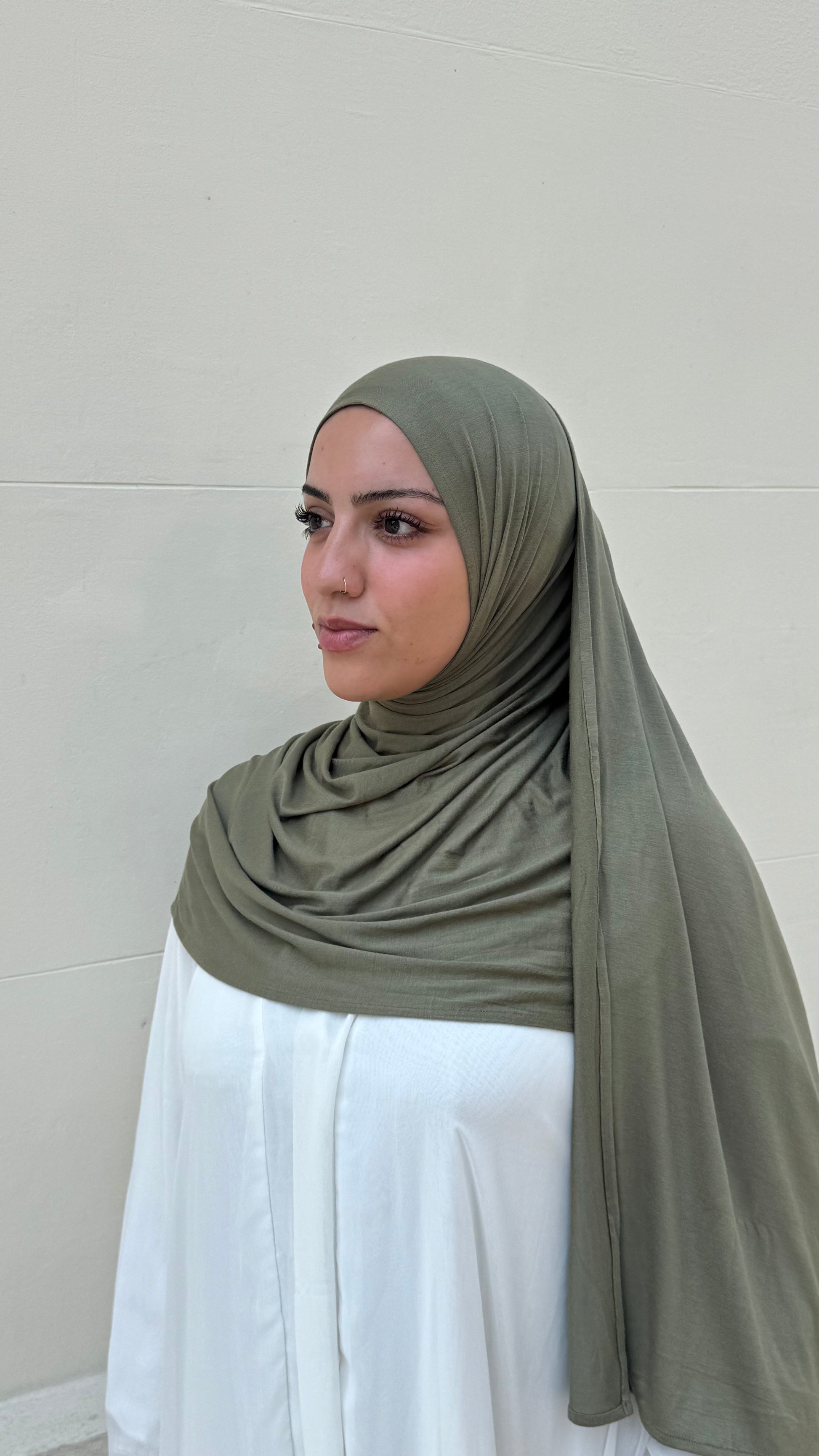 Woman wearing a green hijab and white outfit against a plain background in london
